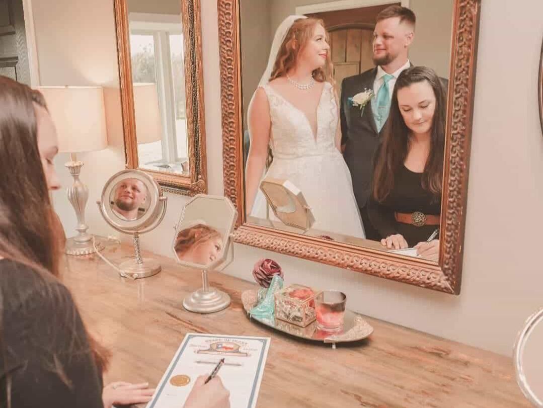Bride and groom's reflection in a mirror above the officiant who is signing the marriage license.